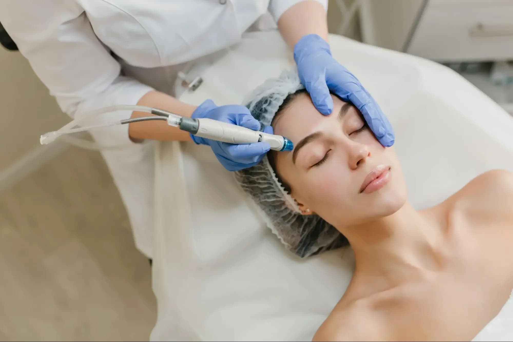 Woman receiving a HydraFacial treatment on her forehead performed by a skincare professional.