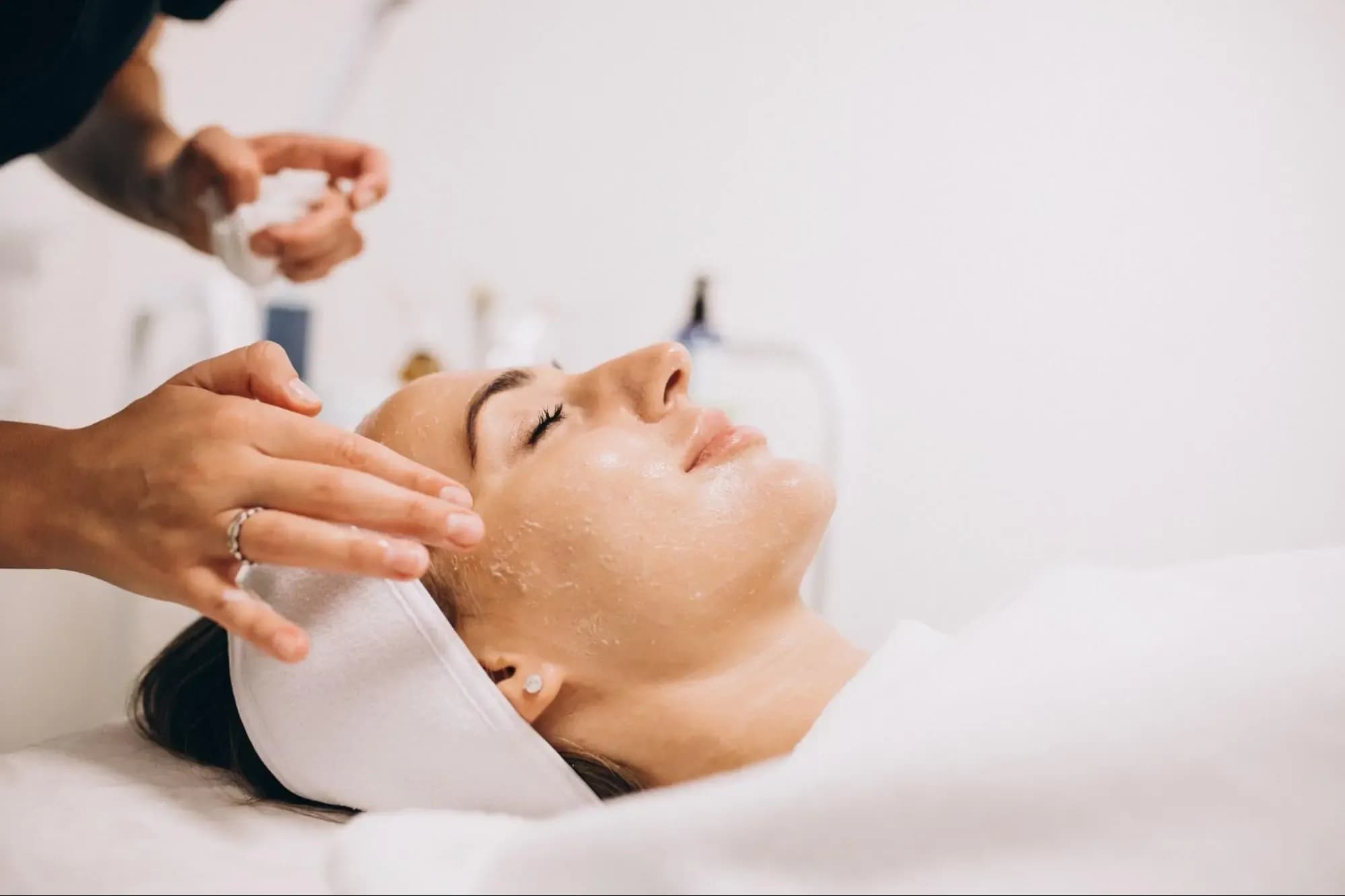 Aesthetician gently cleansing a woman's face during a HydraFacial treatment at a skincare clinic.