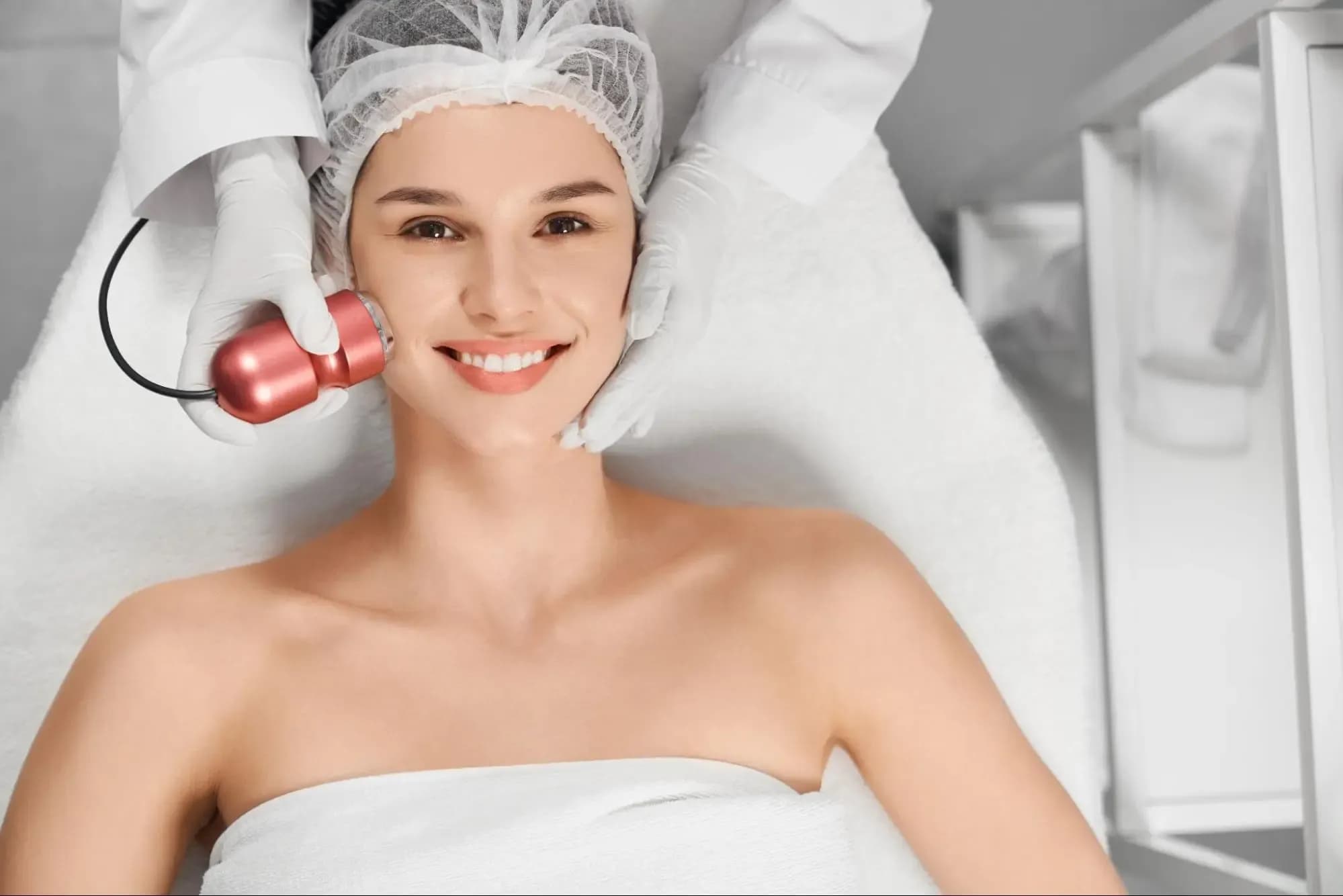 Smiling woman receiving a HydraFacial treatment in a modern aesthetic clinic.