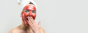 Woman surprised during vampire facial PRP treatment with red serum mask